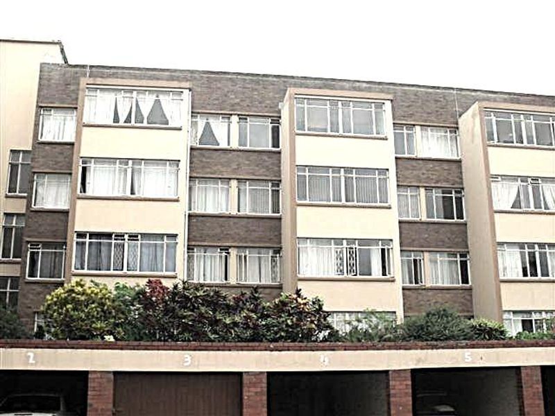 Exterior view of a multi-story apartment building featuring a brick facade, large windows, and ground-level covered parking bays.