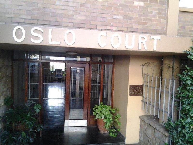 The front entrance of Oslo Court apartment building, featuring a brick facade, security gate, and stone cladding details.