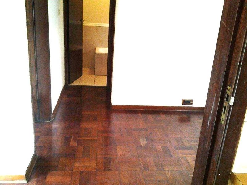 A vacant hallway featuring dark parquet flooring and wooden door frames, leading into a tiled bathroom area.