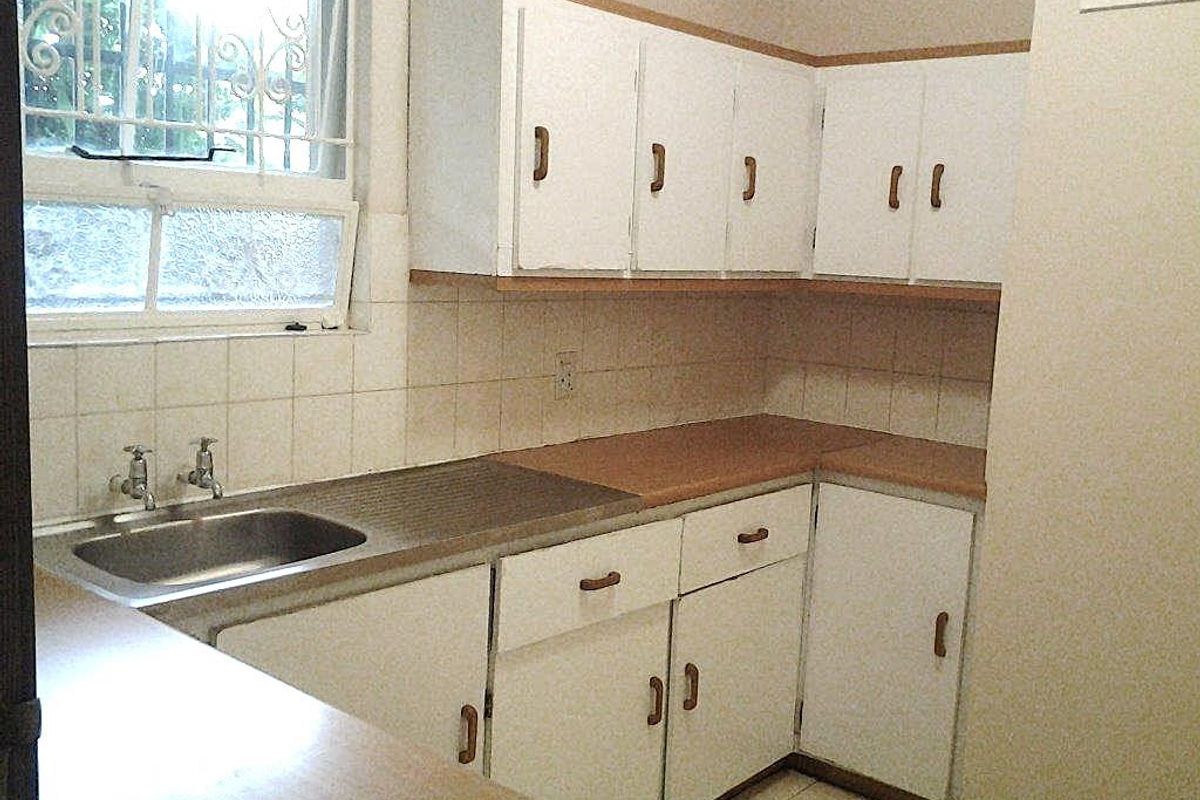 A functional kitchen featuring white built-in cabinetry, laminate countertops, a stainless steel sink, and a tiled backsplash, offering potential for modern updates.