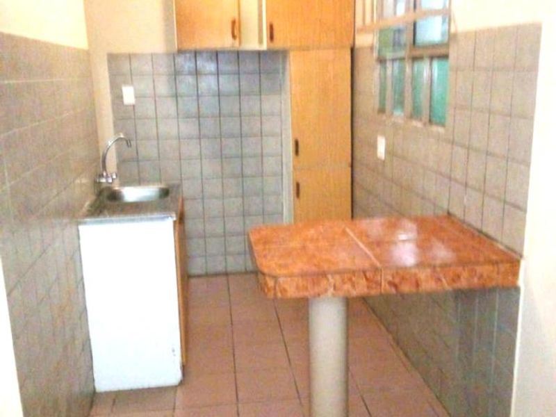 A compact kitchen featuring tiled walls, built-in cabinetry, a sink, and a tiled breakfast counter, currently in need of modernization.