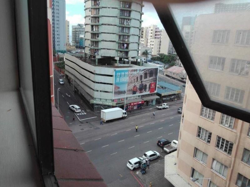An elevated urban view looking out from an apartment window over a busy city street intersection and surrounding high-rise buildings.