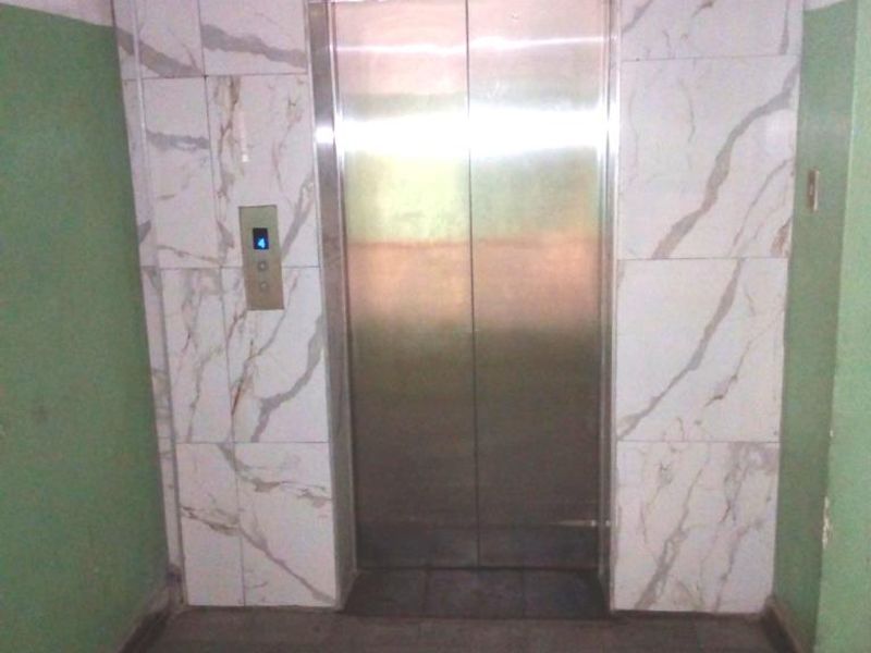 A functional apartment building hallway featuring a stainless steel elevator with marble-effect wall cladding.