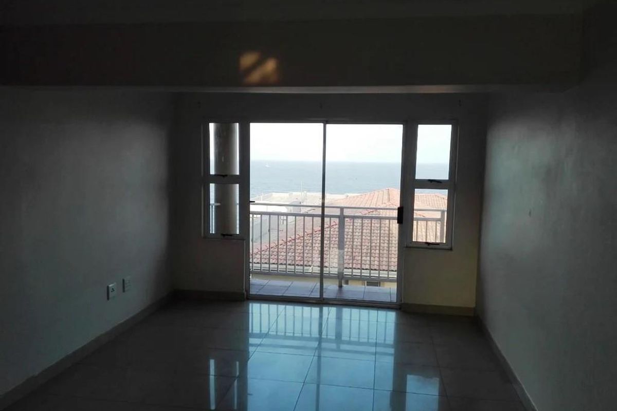 An empty living area featuring tiled flooring and large sliding glass doors that open onto a balcony with ocean views.