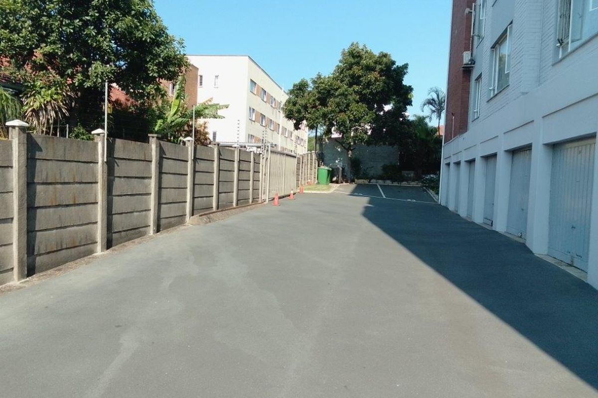 Exterior view of the apartment complex driveway featuring a paved parking area, perimeter concrete wall, and access to ground-level garage units.