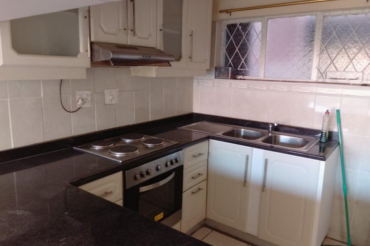 A functional kitchen featuring dark granite countertops, built-in oven, electric hob, extractor fan, and a double stainless steel sink with tiled splashbacks.