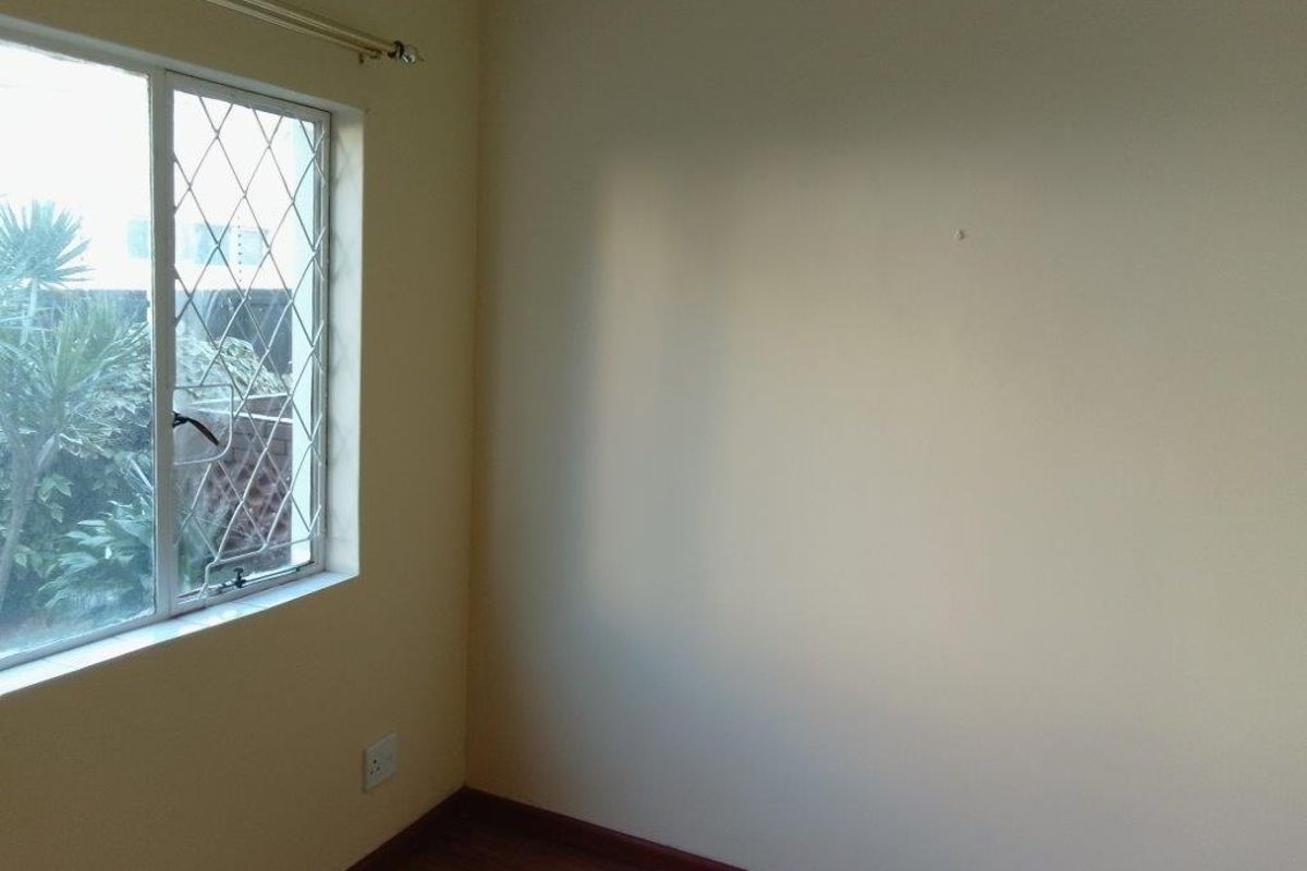 A simple, empty bedroom featuring laminate flooring and a window with security bars, offering a neutral space ready for personalization.