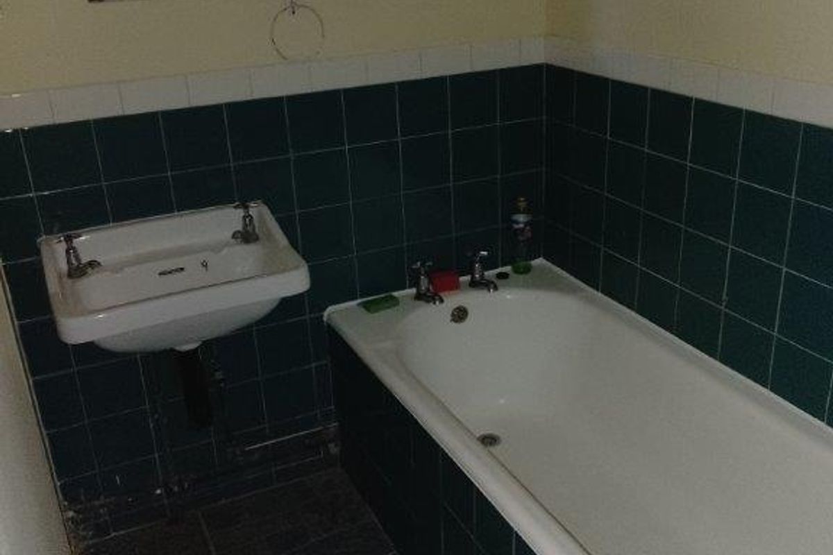 A dated bathroom featuring a standard bathtub, wall-mounted basin, and dark green tiled splashbacks with a leaded glass window.