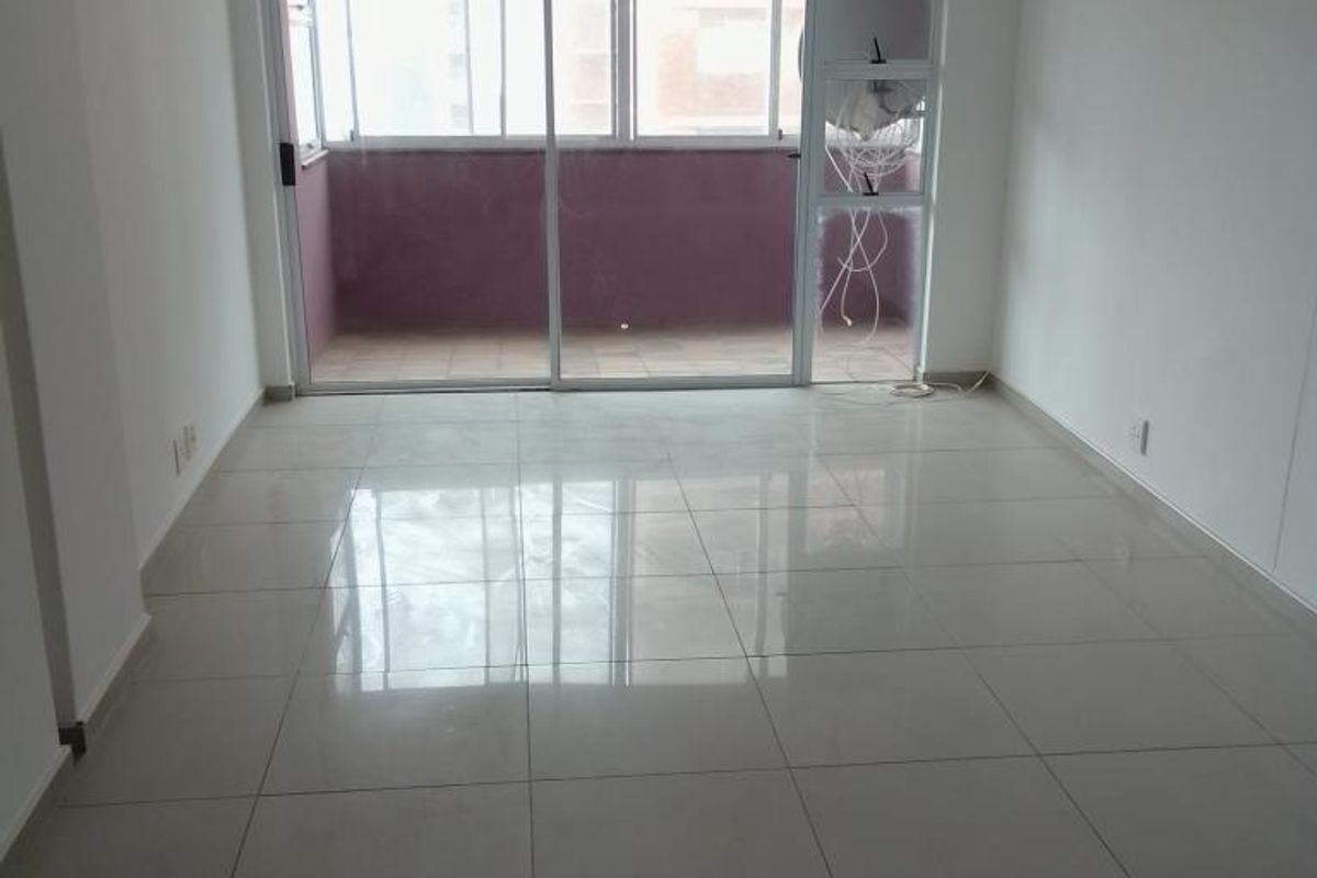 A bright, empty living area featuring large sliding glass doors that open onto a private balcony, finished with neutral ceramic floor tiles throughout.