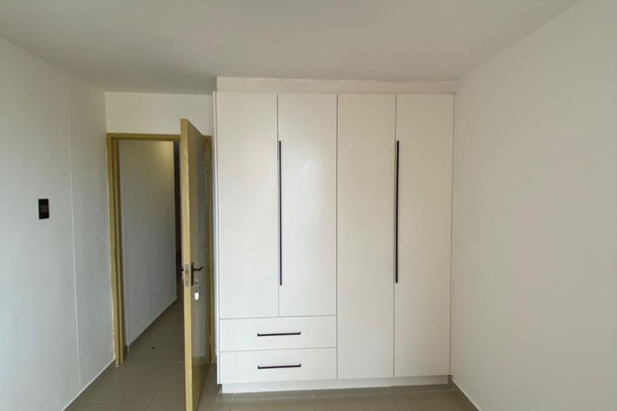 A clean, minimalist bedroom featuring built-in white cabinetry with modern vertical handles and neutral floor tiling.