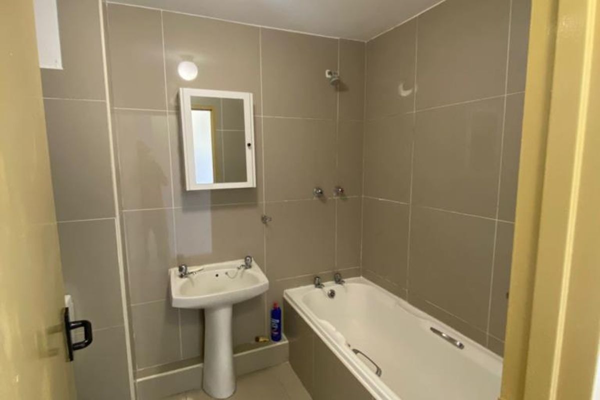 A functional bathroom featuring floor-to-ceiling neutral tiling, a pedestal basin, and a standard bathtub with wall-mounted taps.