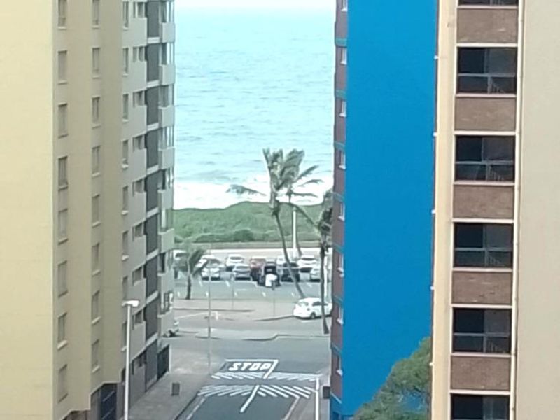 An elevated view looking down a street between two apartment buildings towards the ocean.