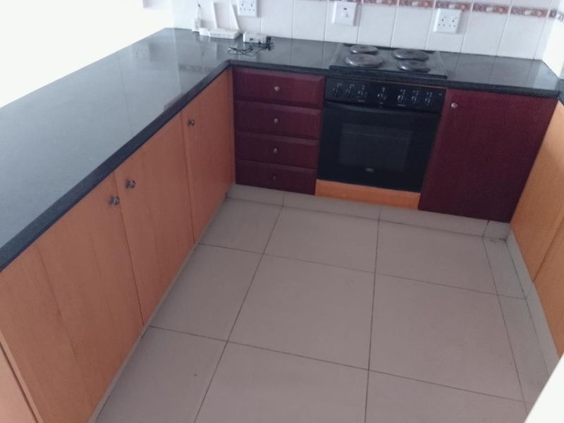 A functional kitchen featuring dark granite countertops, built-in oven and hob, and two-tone wooden cabinetry with tiled flooring.