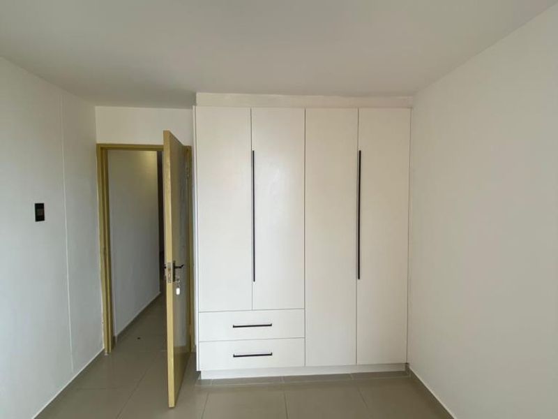 A clean, minimalist bedroom featuring built-in white cabinetry with modern vertical handles and neutral floor tiling.
