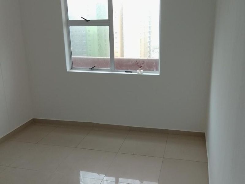 A bright, empty bedroom featuring neutral tiled flooring and a large window providing natural light and an urban view.