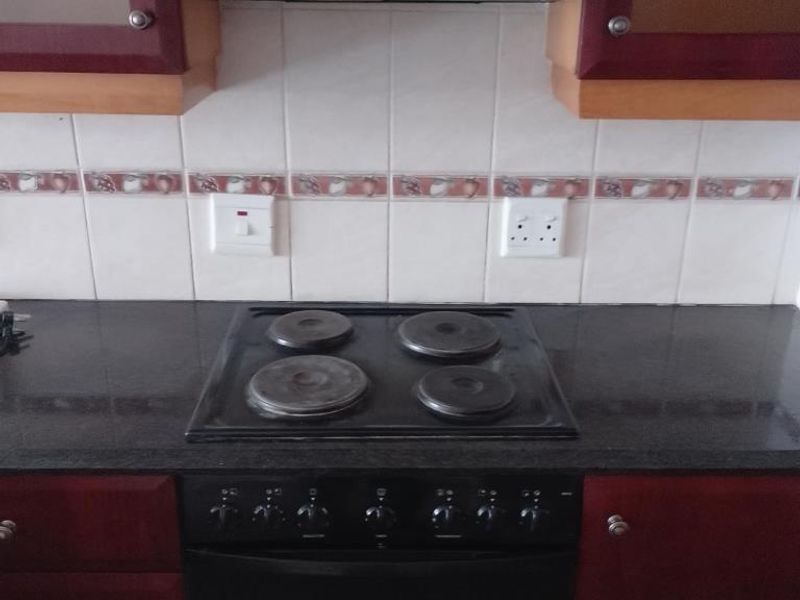 A kitchen workspace featuring a built-in electric hob, oven, extractor fan, and tiled backsplash with dark cabinetry.