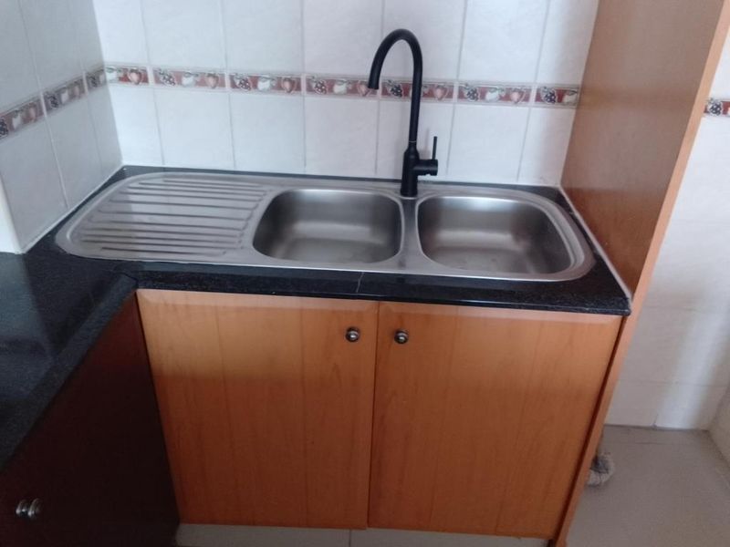A functional kitchen sink area featuring a stainless steel double basin, modern black faucet, dark stone countertop, and wood-finish cabinetry with a decorative tile backsplash.