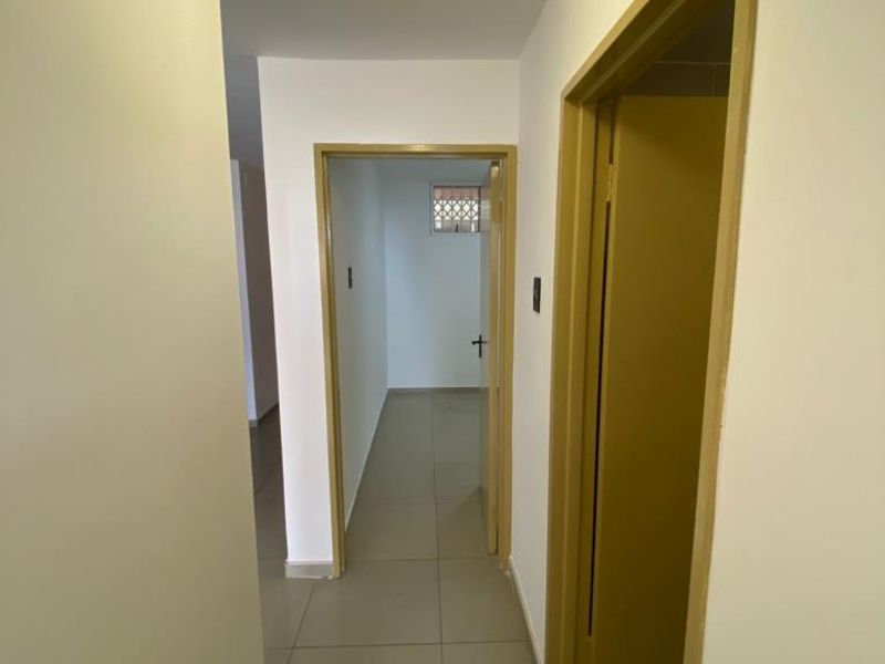 A clean, neutral hallway featuring tiled flooring and access to multiple rooms, providing a functional transition space within the apartment.