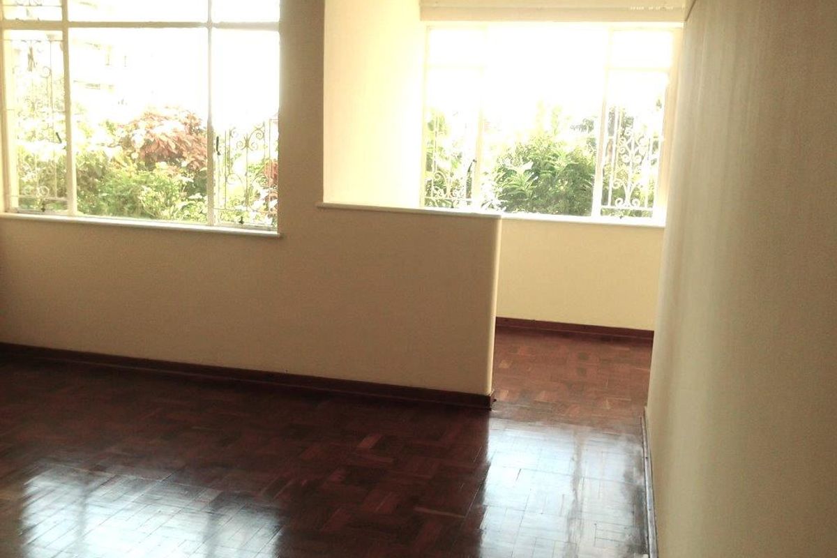 An empty living room featuring polished parquet flooring, large windows providing natural light, and a half-height partition wall separating the space.