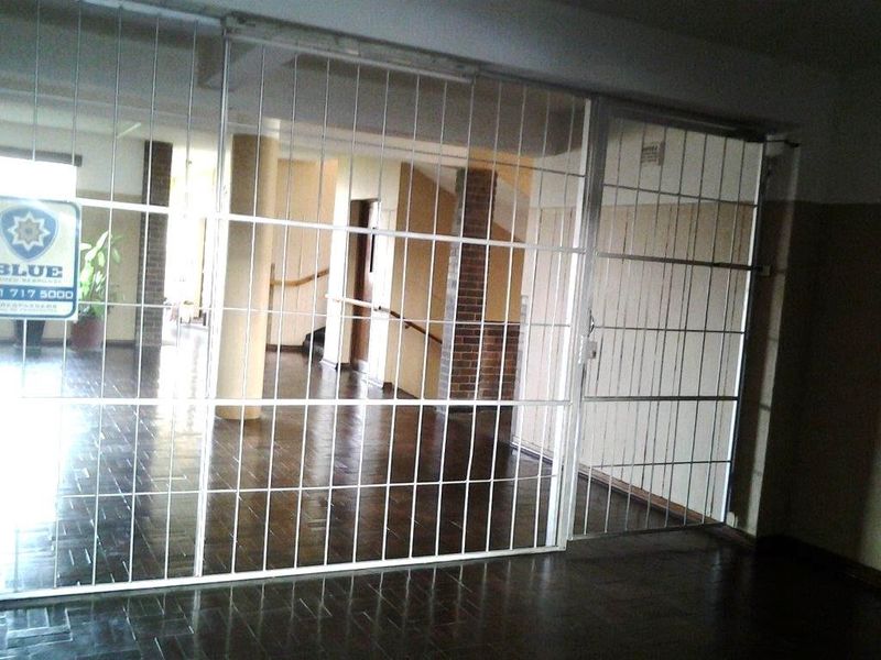 A vacant hallway area featuring parquet flooring, a brick pillar, and a large security gate partition.