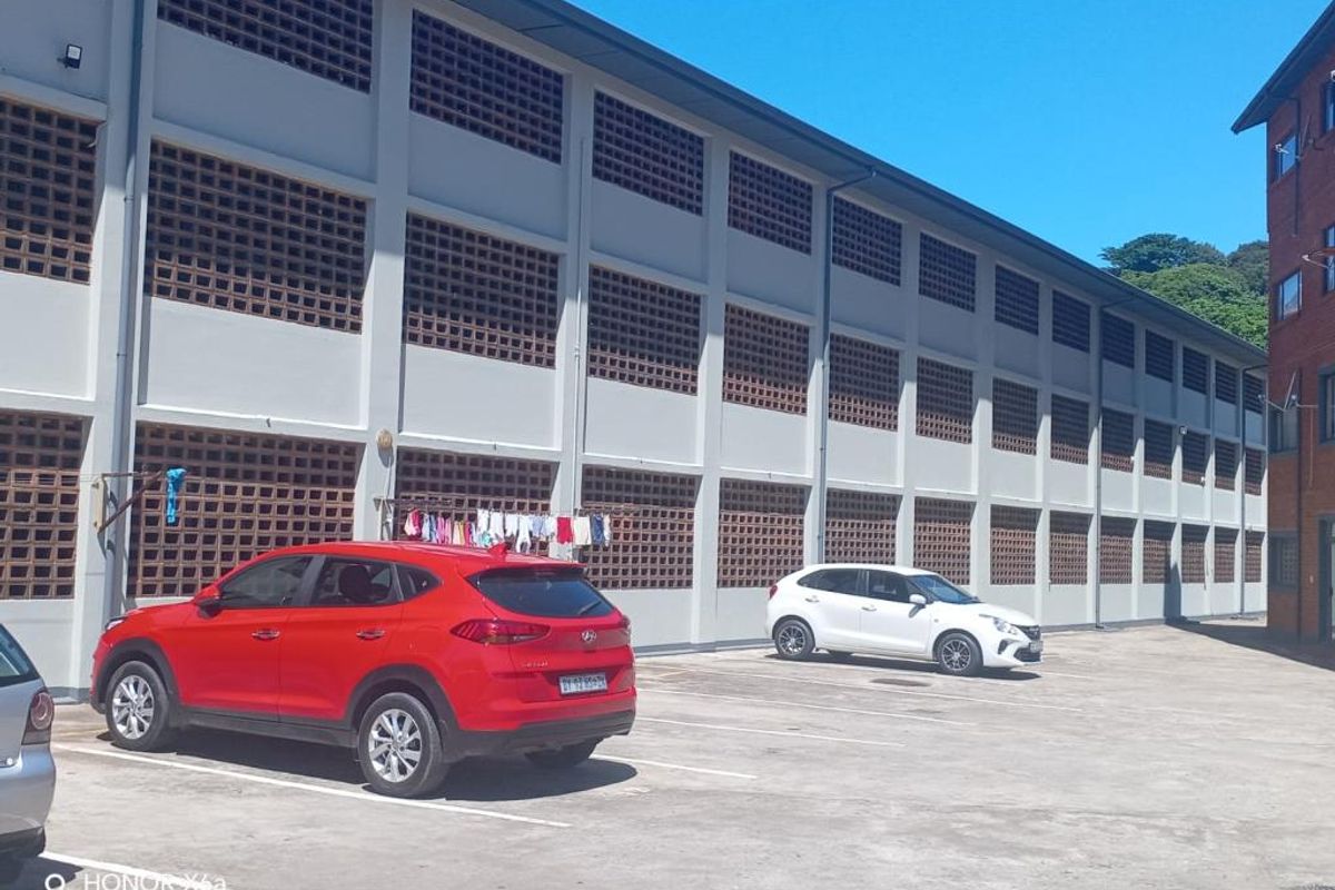 Exterior view of the apartment building facade featuring concrete block ventilation screens and a paved parking area.
