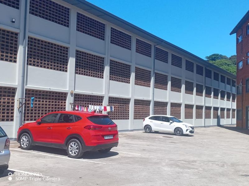 Exterior view of the apartment building facade featuring concrete block ventilation screens and a paved parking area.