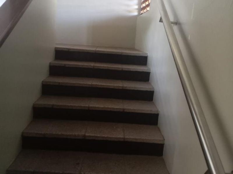 A functional interior staircase featuring tiled steps, a wooden handrail on one side, and a metal handrail on the other.