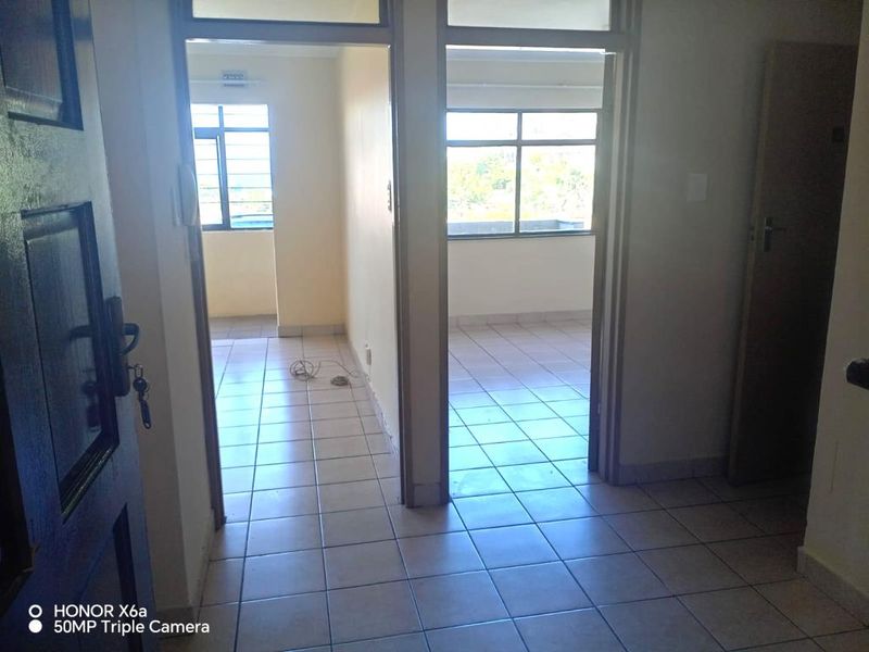 A view from the entrance hallway looking into two adjacent rooms, featuring tiled flooring and large windows providing natural light.