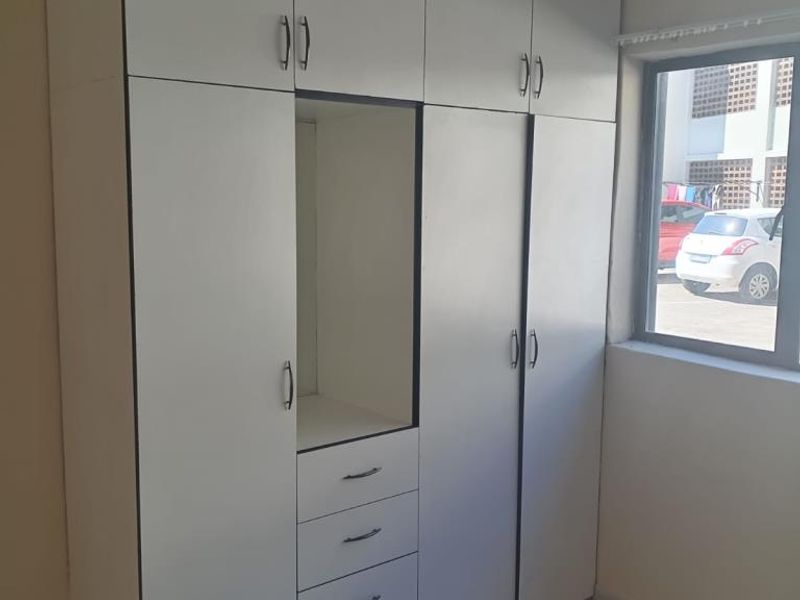 A bedroom featuring built-in white cabinetry with integrated drawers and shelving, complemented by tiled flooring and a window providing natural light.