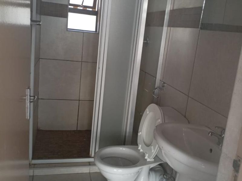 A functional bathroom featuring a pedestal basin, a standard toilet, and a shower enclosure with a tiled interior.