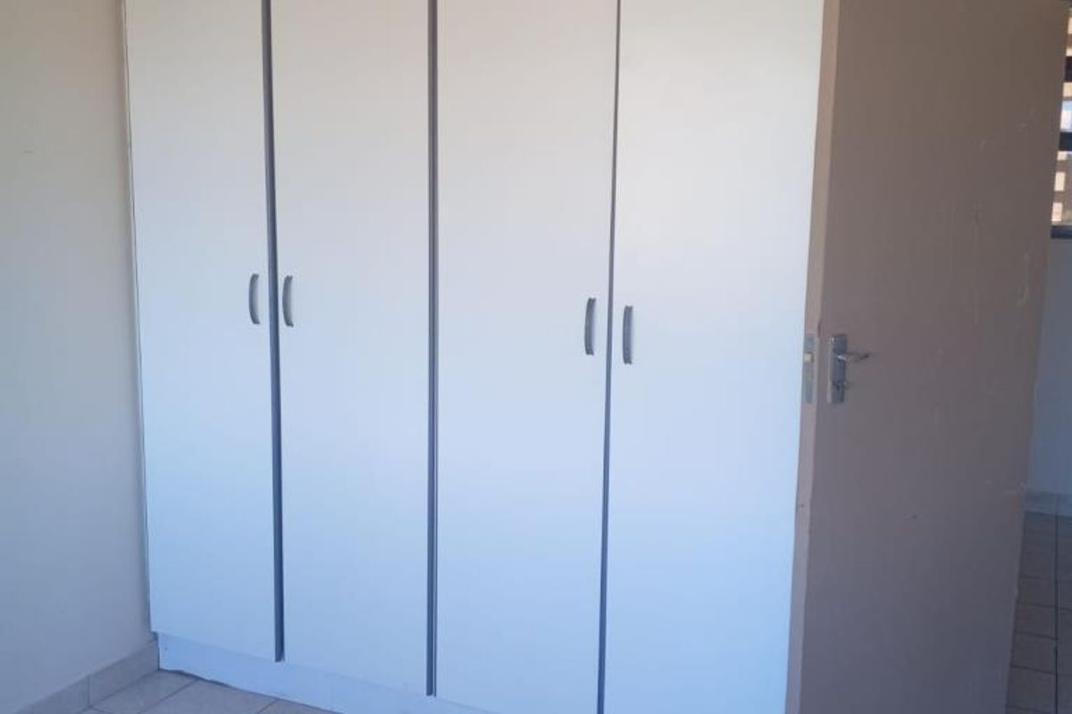 A bedroom featuring built-in white cabinetry with vertical handles and tiled flooring.