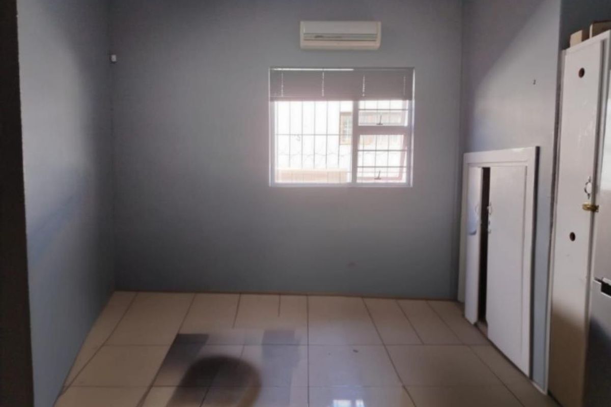 A vacant room featuring tiled flooring, a wall-mounted air conditioning unit, security bars on the window, and built-in storage cabinetry.