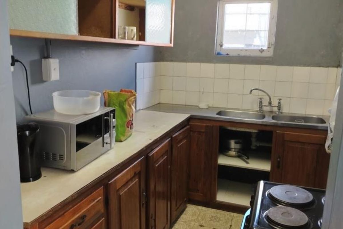 A compact kitchen featuring wooden cabinetry, a double basin sink, tiled splashback, and a freestanding stove.
