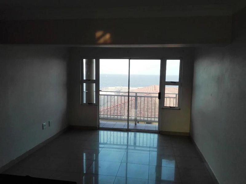 An empty living area featuring tiled flooring and large sliding glass doors that open onto a balcony with ocean views.