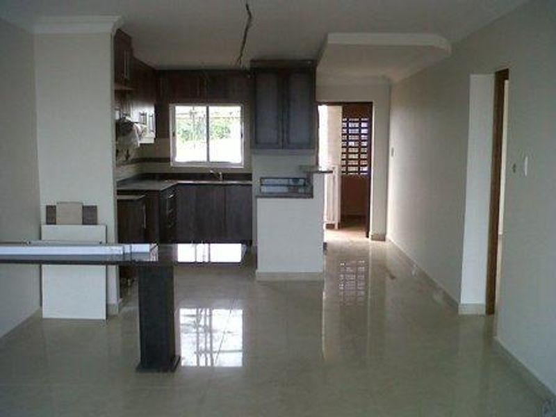 An open-plan living and kitchen area featuring tiled flooring, dark wood-toned cabinetry, and a breakfast counter, currently in an unfinished state.