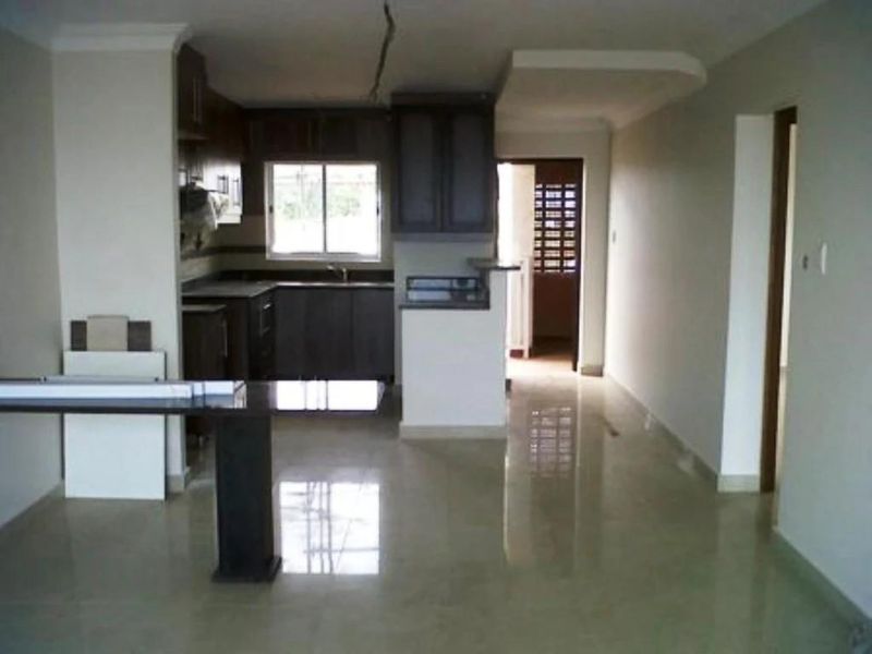 Open plan kitchen and living area featuring dark cabinetry, tiled flooring, and a breakfast bar counter in a neutral apartment setting.