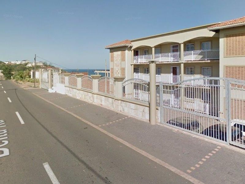 Street view of the apartment complex exterior, featuring a secure gated entrance, perimeter wall, and multi-level balconies.
