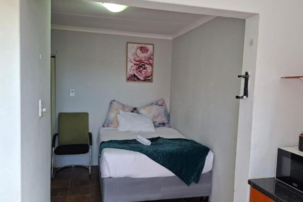 An open-plan studio apartment featuring a combined sleeping and kitchen area with tiled flooring and functional built-in cabinetry.