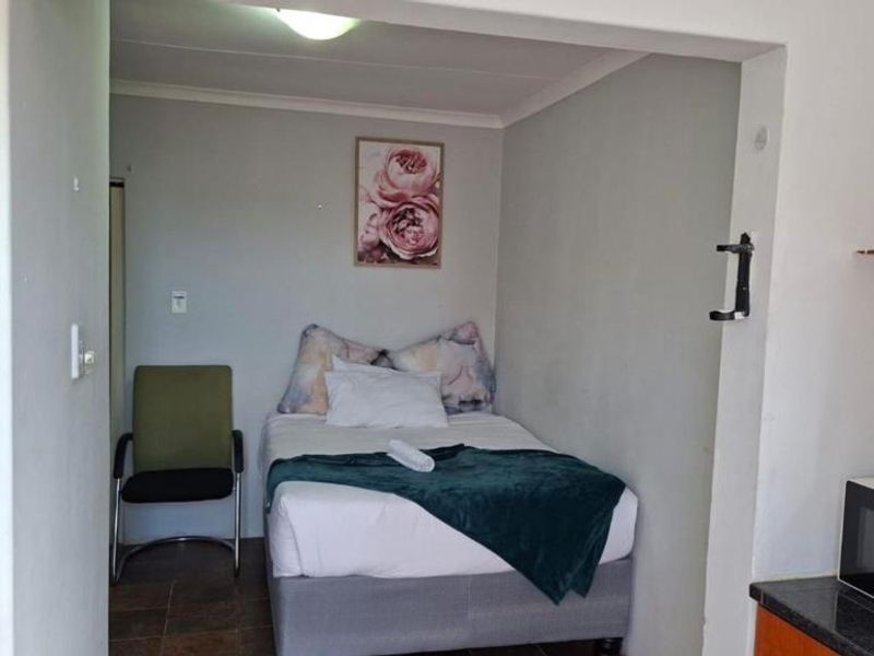 An open-plan studio apartment featuring a combined sleeping and kitchen area with tiled flooring and functional built-in cabinetry.