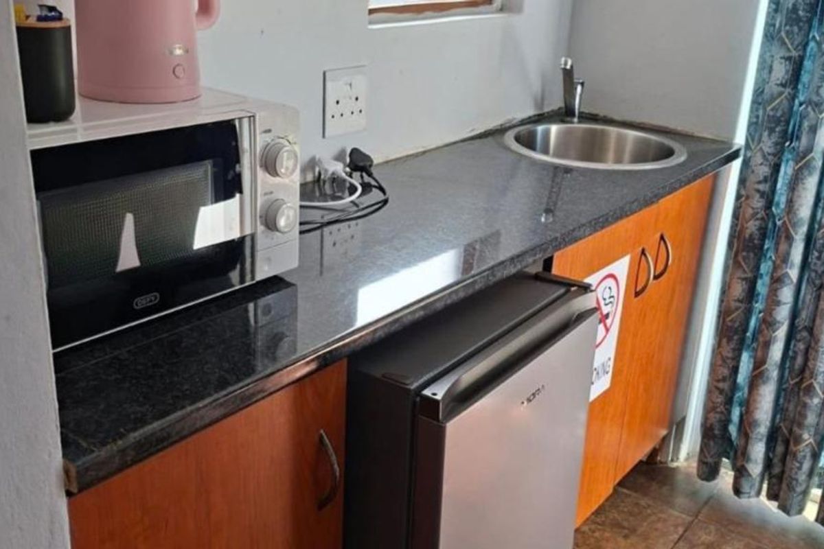 Compact scullery area featuring granite countertops, built-in cabinetry, and a stainless steel sink, providing functional prep space.