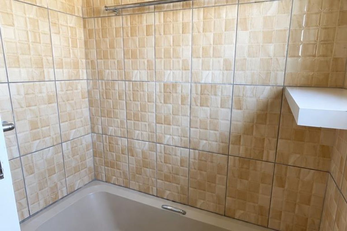 A bathroom featuring a built-in bathtub with wall-mounted shower fixtures and dated ceramic wall tiling.