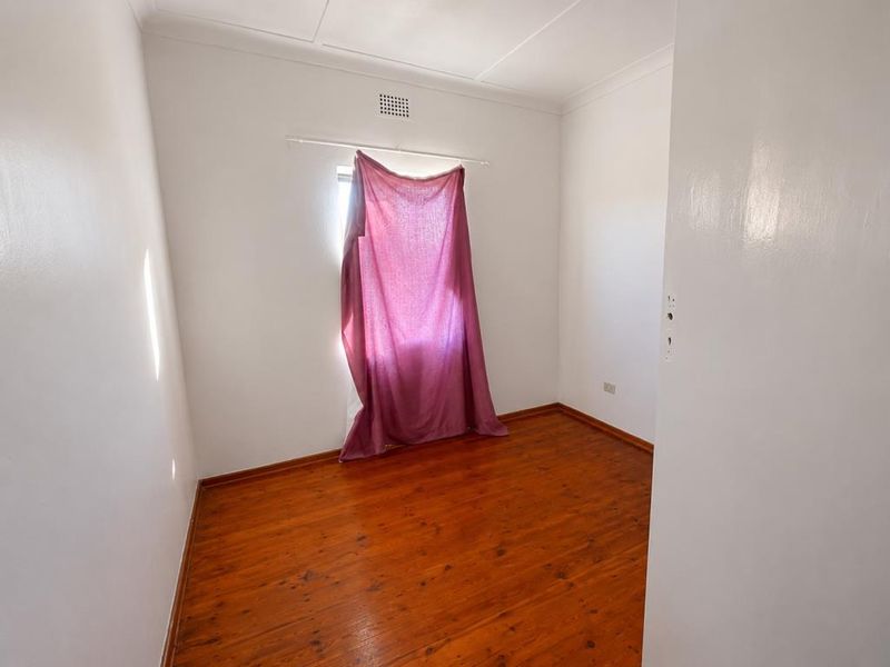 A vacant bedroom featuring polished timber flooring and a doorway leading to an adjacent tiled bathroom.