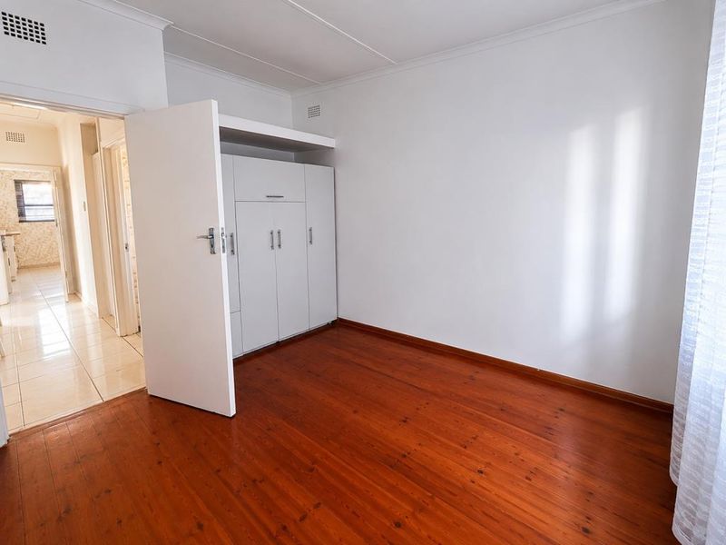 A vacant bedroom featuring polished timber flooring, white painted walls, and a ceiling vent.