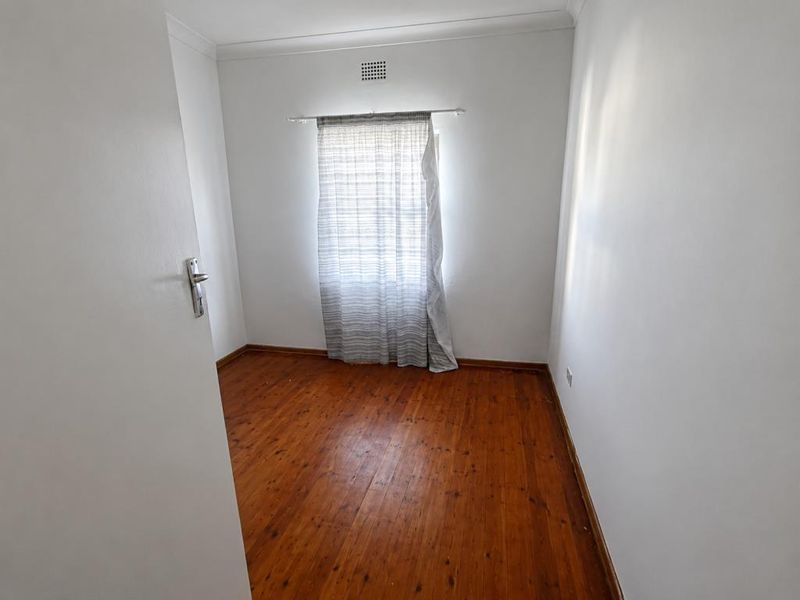 A bright bedroom featuring polished wooden flooring and built-in cabinetry, with a view leading into an adjacent tiled hallway.