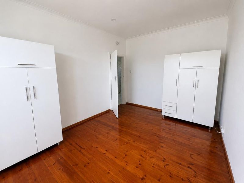 A vacant bedroom featuring polished timber flooring, white walls, and a window with a curtain rod.