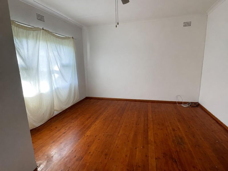 A bedroom featuring polished timber flooring, white walls, and two built-in white wardrobes, with a doorway leading to an adjacent room.
