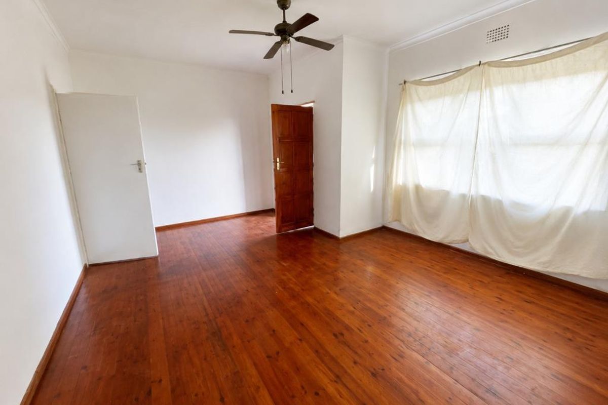 A bright, empty bedroom featuring polished timber flooring, a ceiling fan, and direct access to an outdoor area through a wooden door.