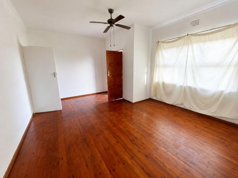 A bright, empty bedroom featuring polished timber flooring, a ceiling fan, and direct access to an outdoor area through a wooden door.