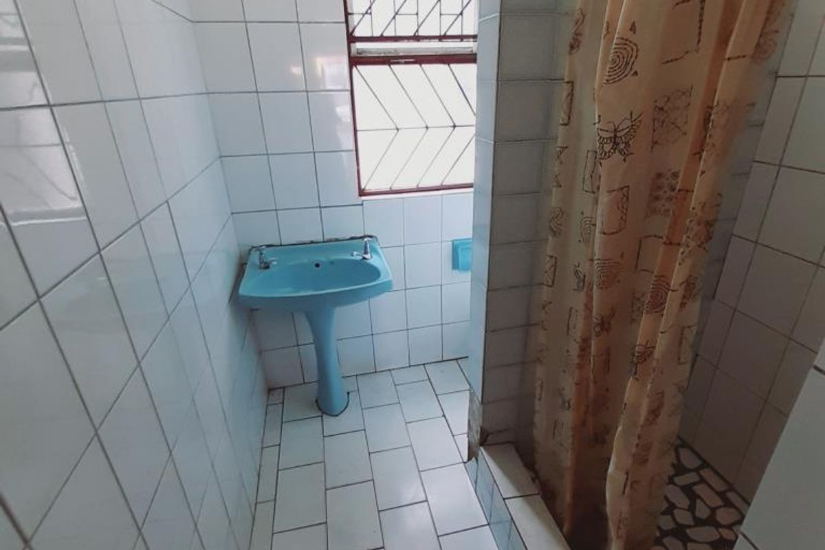 A functional bathroom featuring a blue pedestal basin, tiled walls and flooring, and a shower area with a privacy curtain.