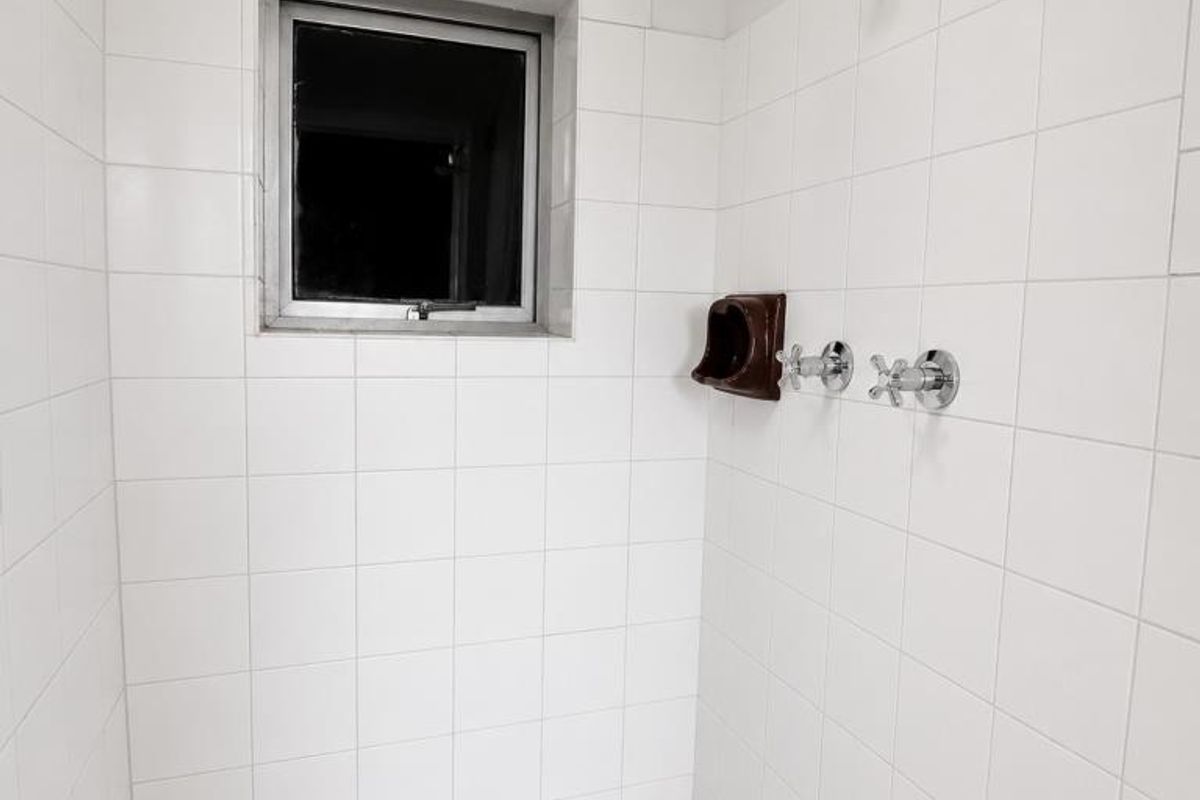 A functional shower enclosure featuring white wall tiles, a mosaic-style floor, and a built-in soap dish with chrome fixtures.